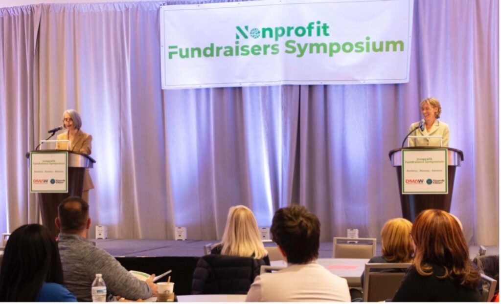Donna Tschiffely & Shannon McCracken speaking on a stage at the Nonprofit Fundraisers Symposium. 
